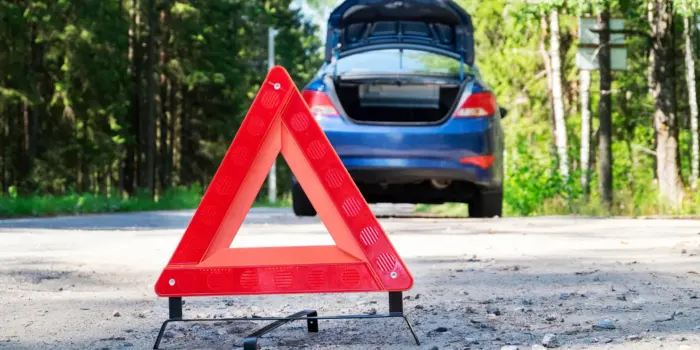 A blue car broken down on side of the road with an orange hazard triangle behind it