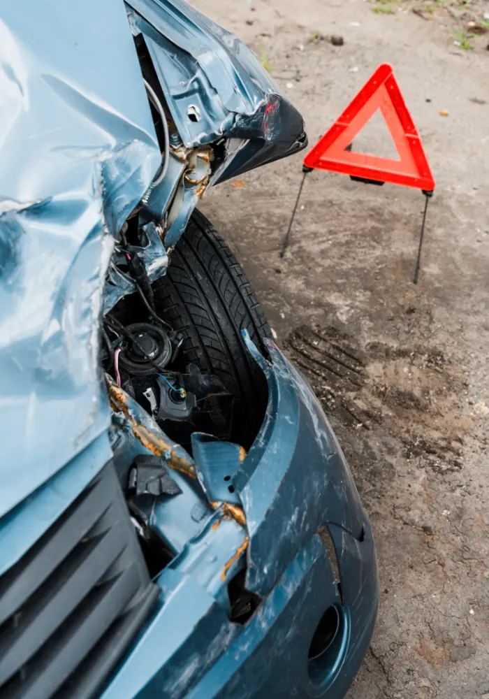 A blue car that is wrecked on the front with an orange hazard triangle