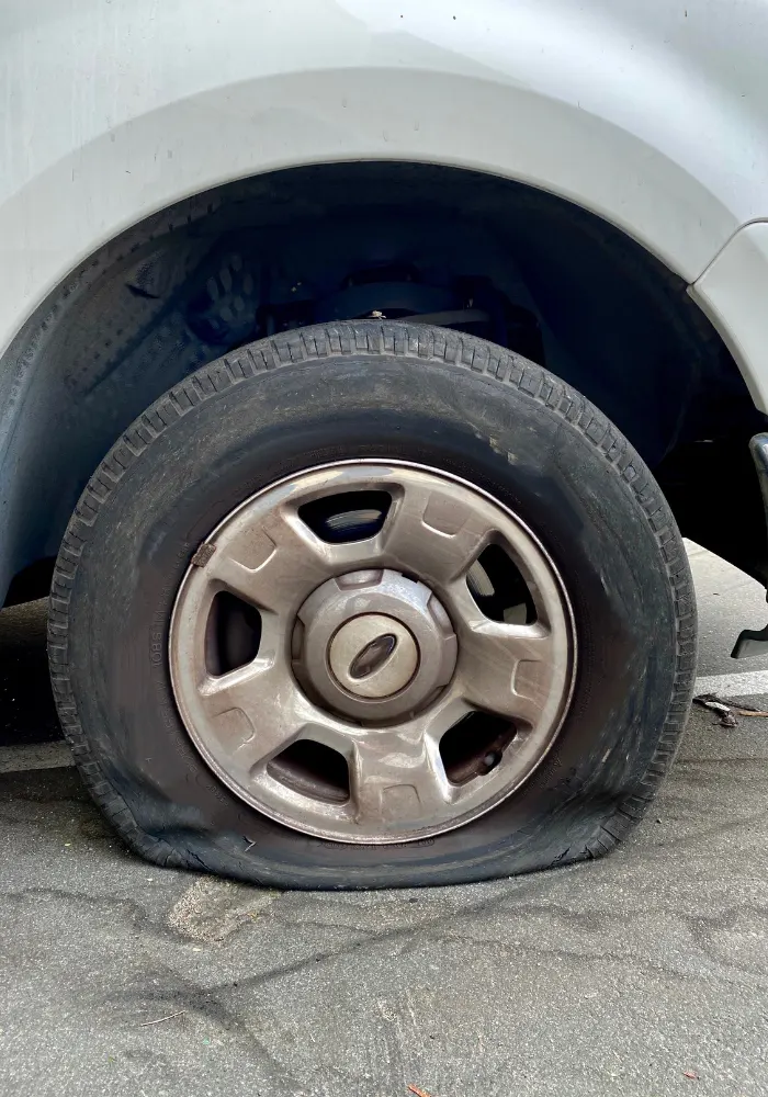 A silver car on the side of the road with a flat tire in the front