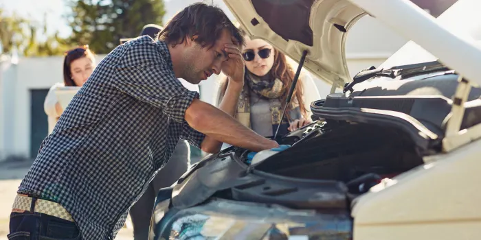 A family whose car has broken down on side of the road, with the man looking at the engine discouragingly